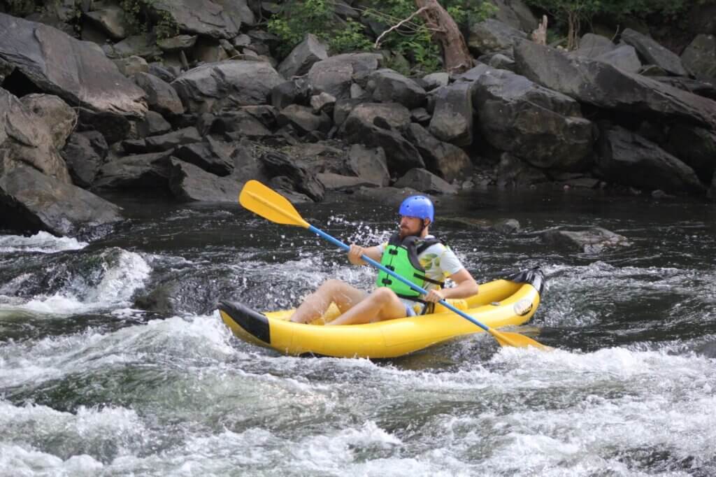 Man in green life vest paddles down Class 3 rapids in inflatable yellow kayak